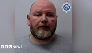 Police custody image of Kieran Cameron. He has a beard and is wearing a grey sweatshirt.
