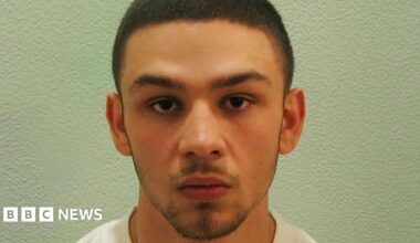 A custody photo of Jake Fahri. He has short brown hair, a moustache and short beard.