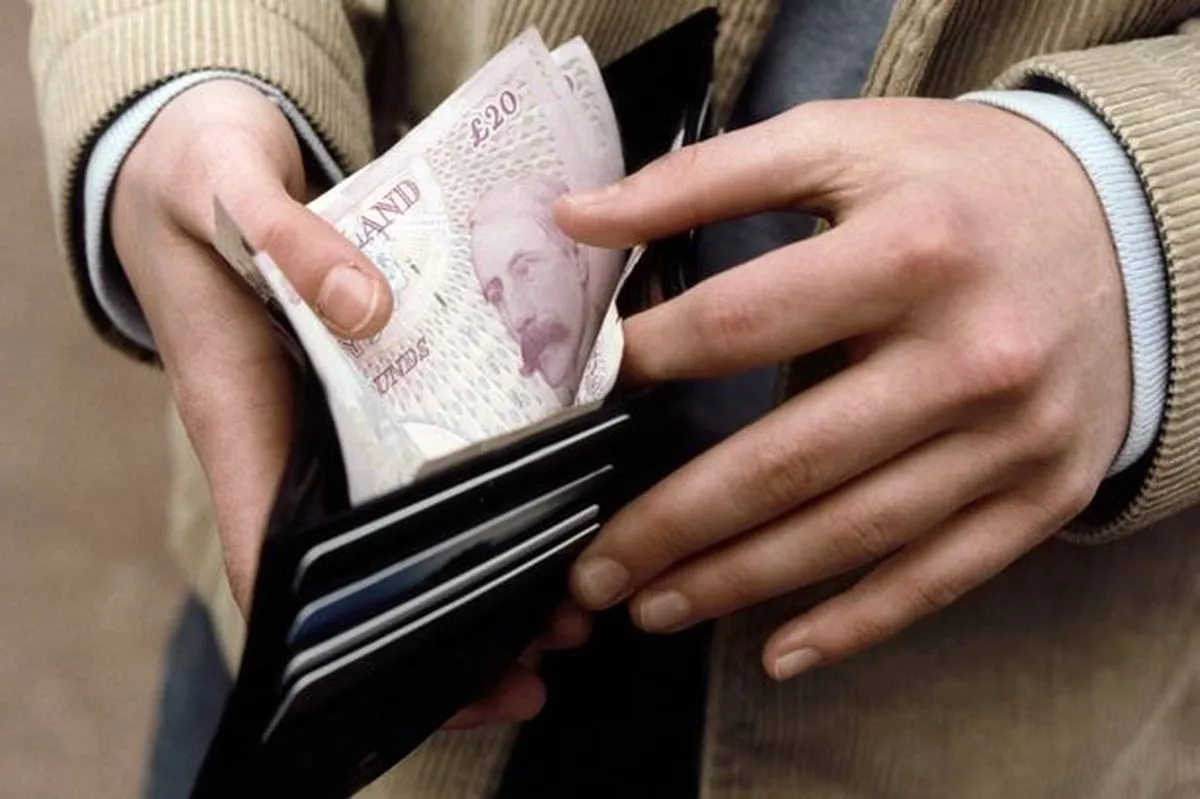 A man is holding open his wallet showing the cash contents 