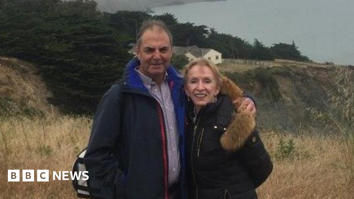 Terry, on the left, is wearing a patterned shirt and a black coat and has short brown hair. Wendy J. Tomlin-Hess is on the right and has short dark blonde hair, and is wearing a black coat. They are stood on a hill.
