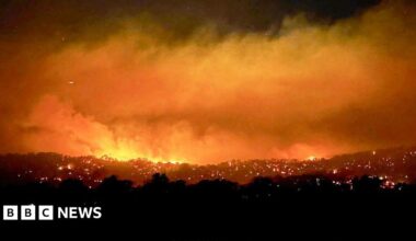 A large fire with smoke and an bright orange haze over a large bush area