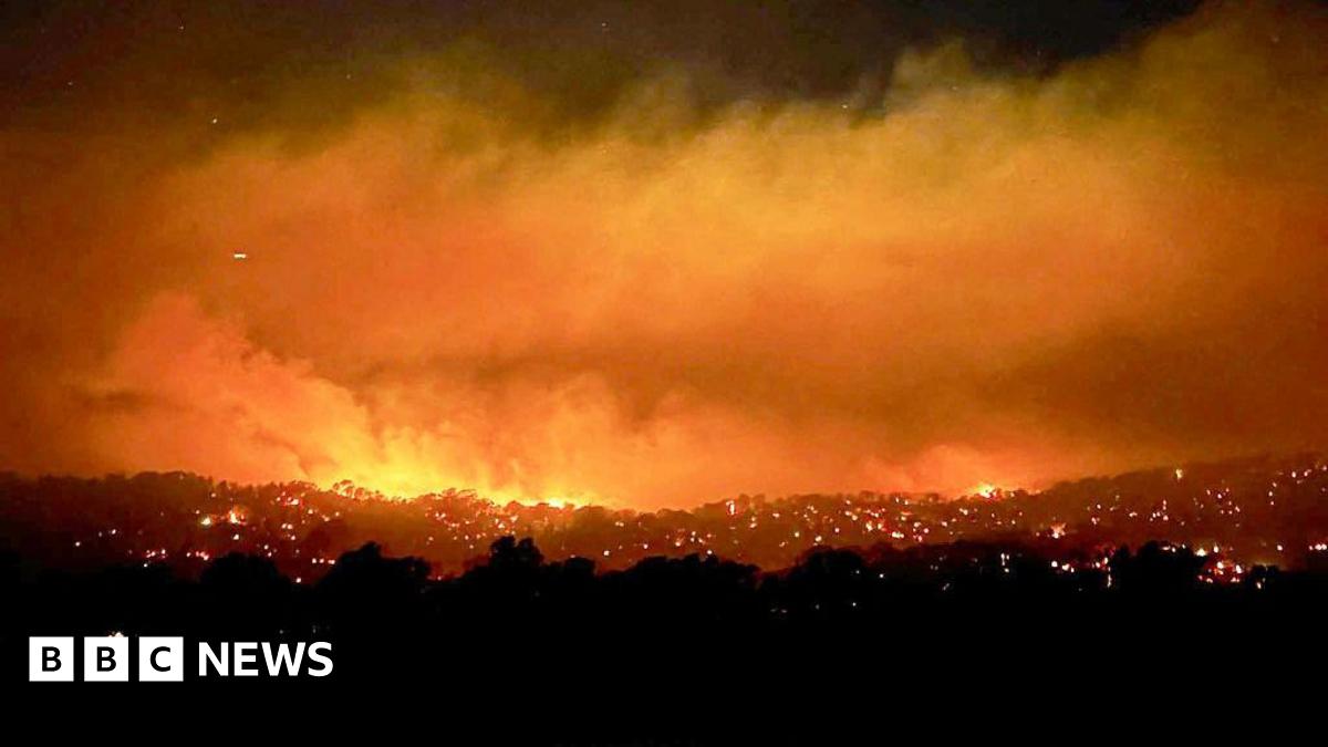 A large fire with smoke and an bright orange haze over a large bush area