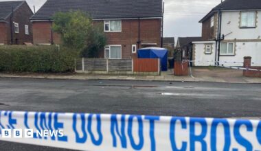 The front of a semi-detached house with a blue forensic police tent in the front yard. Blue and white police tape is visible in the foreground