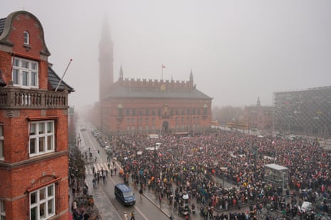 A large crowd gathers in front of the red brick City Hall in Copenhagen, Denmark on a foggy grey day. 