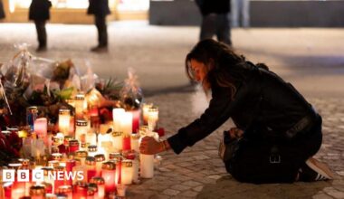A woman kneels on the floor lighting a candle next to a pile of tributes including flowers and other lit candles outside Le Constellation bar in Crans-Montana.