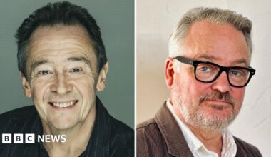 A very young Paul Whitehouse and Charlie Higson - Whitehouse, with a fine head of dark brown hair, wears a grey sweatshirt while Higson, with very dark hair, slicked back, sits in a grey shirt, jeans and a leather jacket.