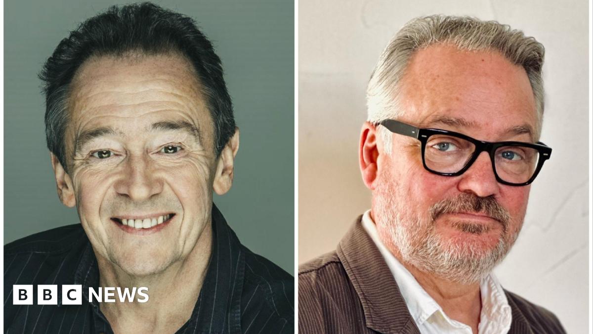 A very young Paul Whitehouse and Charlie Higson - Whitehouse, with a fine head of dark brown hair, wears a grey sweatshirt while Higson, with very dark hair, slicked back, sits in a grey shirt, jeans and a leather jacket.