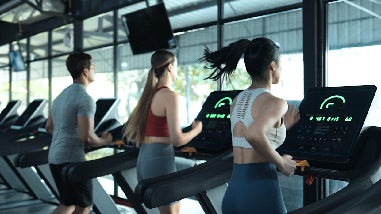 Three people running on treadmills in a gym setting