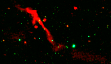 A red ribbon of radio energy blasts out of a black hole on a black background