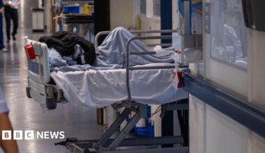 A patient bed is being pulled through a doorway on an NHS hospital ward.