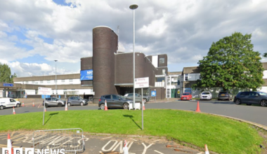 A large hospital building, with several vehicles parked in front