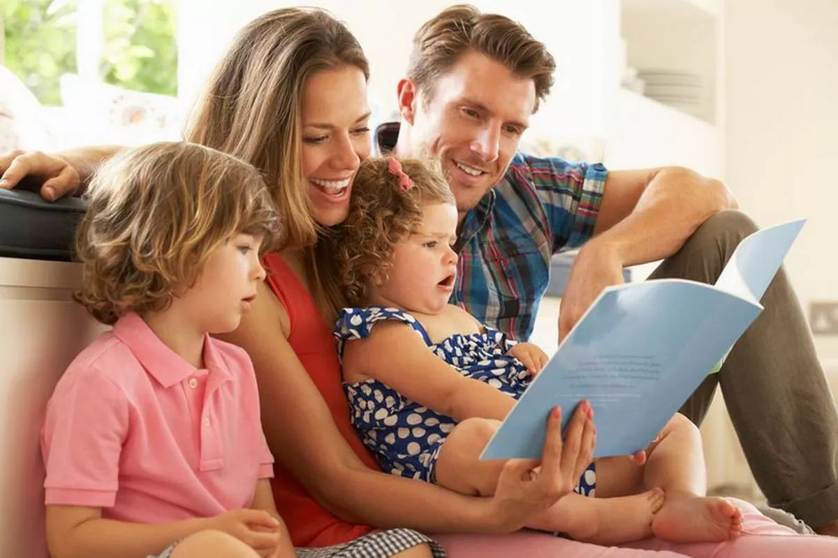A family are sitting on the floor reading a book.