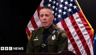 Jacqui Furneaux sitting on her motorbike smiling outside a rundown house on her travels in India