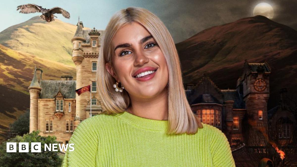 Livi Deane standing in front of the castle where The Traitors is filmed. An owl soars over the mountains in the background.