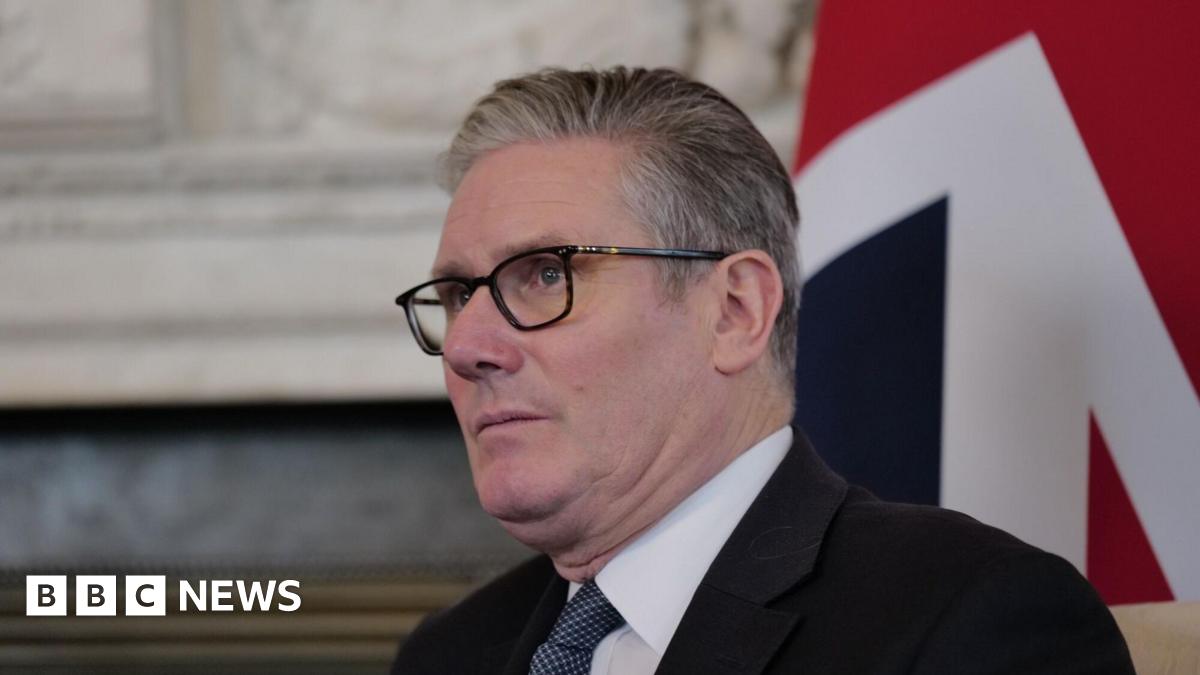 Keir Starmer wearing a suit in front of a union flag. He is looking into the distance