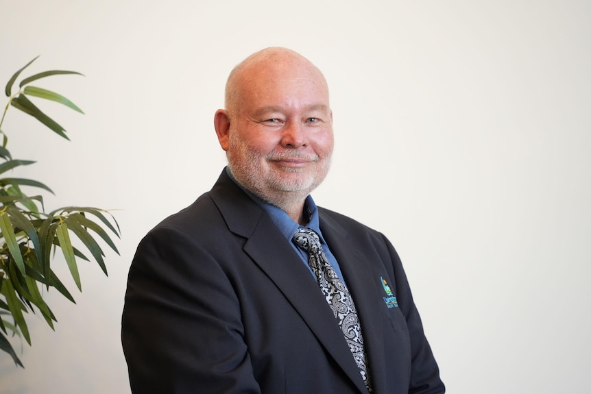 A man with a bald head and short beard and wearing a suit smiles at the camera.