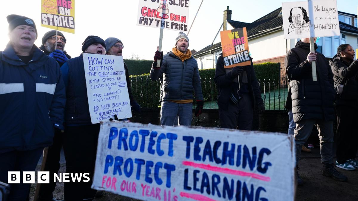 A group of people in winter clothing hold up sign supporting the strike action. A sign in the foreground reads: "Protect teaching, protect learning."