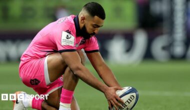 Zack Henry placing the rugby ball down on a tee ready for a kick at goal while dressed in Stade Francais' all-pink kit