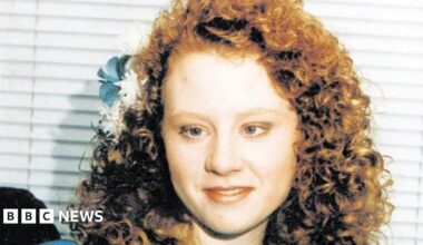 A family image of a young girl, dressed for a wedding in a bridesmaid's dress in blue, with curly red hair and blue and white flowers in her hair.
