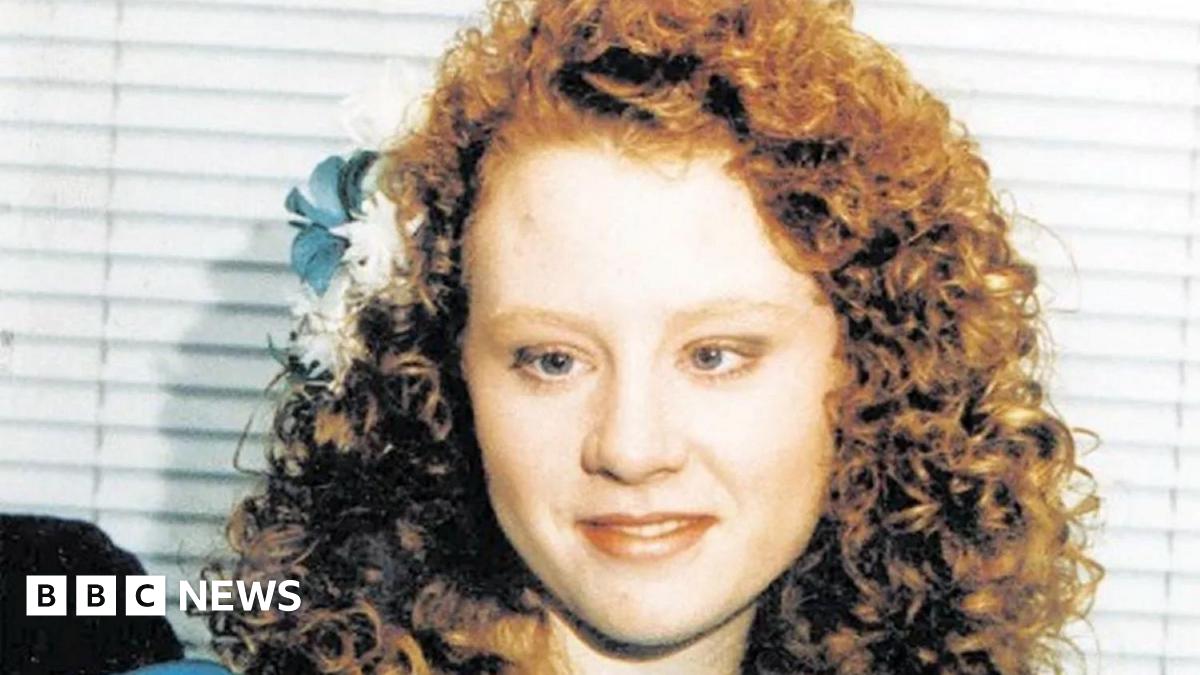 A family image of a young girl, dressed for a wedding in a bridesmaid's dress in blue, with curly red hair and blue and white flowers in her hair.