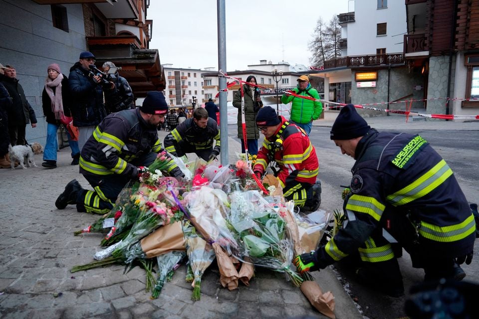 Firefighters lay flowers near the sealed off Le Constellation bar in Crans-Montana, Swiss Alps, Switzerland, Friday, Jan. 2, 2026, where a devastating fire left dead and injured during the New Year's celebrations. (AP Photo/Baz Ratner)