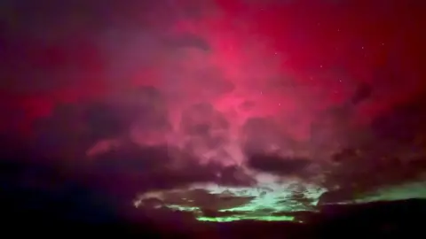 CLAIRE ADAM Green and red northern lights over the skies 