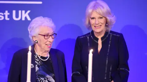 AFP via Getty Images  Eva Schloss MBE, step-sister of Anne Frank and Honorary President of the Anne Frank Trust UK and Camilla, Duchess of Cornwall take part in a candle lighting ceremony during a reception to mark Holocaust memorial day