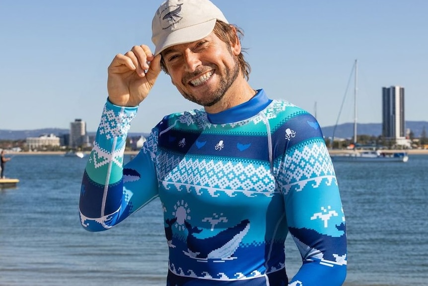Man holding his hat on a beach.