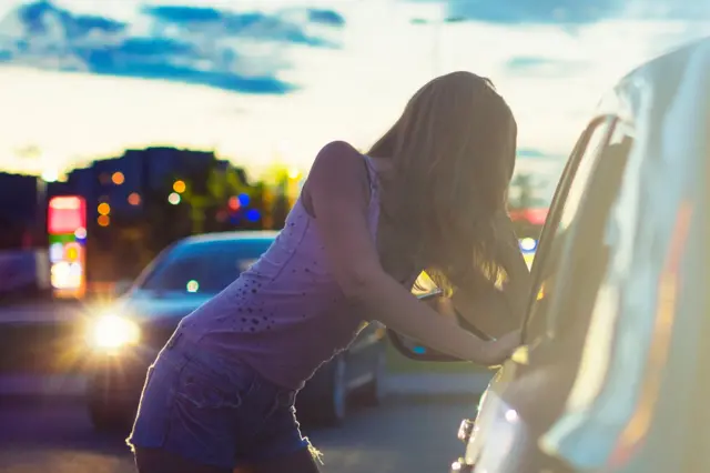 A woman rests on a vehicle and looks into it