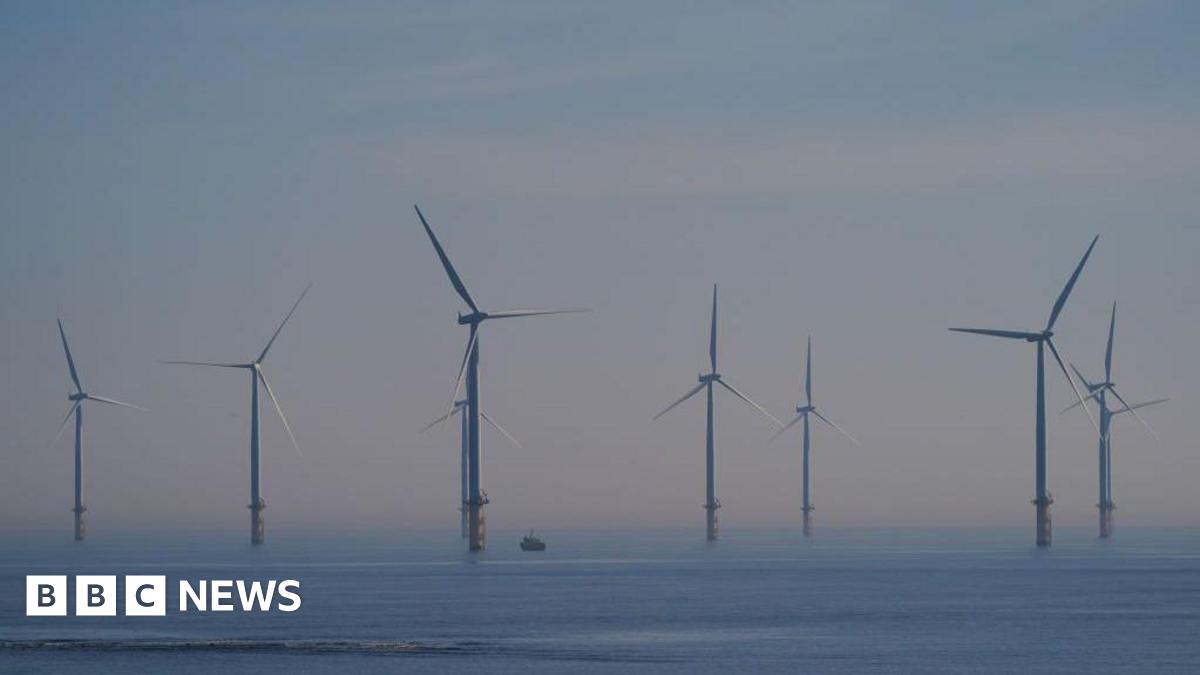 Millie Bobby Brown and David Harbour in character as Eleven and Jim Hopper. Eleven wears red shorts over grey leggings and a grey jumper. Jim Hopper wears a black leather jacket, a black beanie hat and dark trousers.They are speaking to director Frank Darabont on the set of Stranger Things. There is a vintage advertisement posted in the background with debrief on the ground.