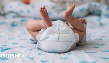Newborn baby lying on a bed but view is of their raised legs and nappy