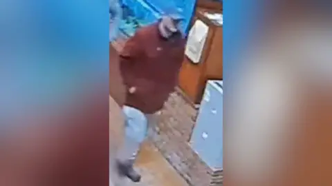 Police handout Matthew Armstrong is wearing a burgundy/orange coat, grey cap, grey tracksuit suit bottoms with blue on the side, and black boots. He is walking on a street, and is captured on CCTV.