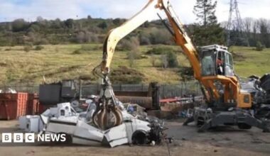 A white car being crushed in a yard