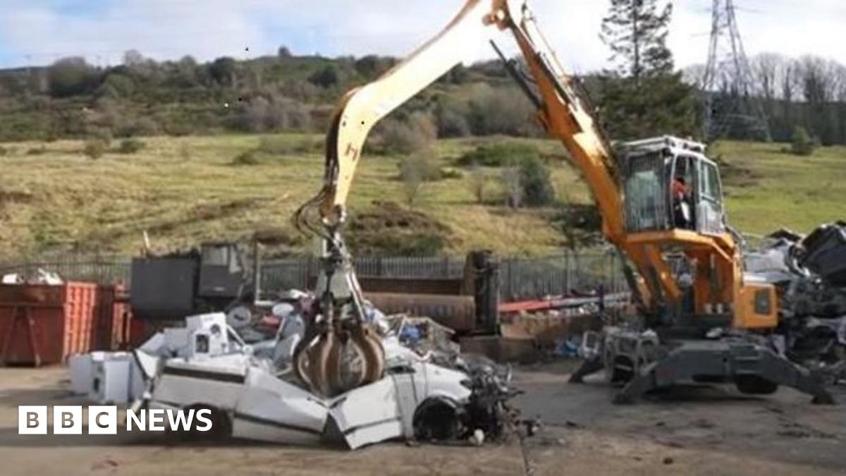 A white car being crushed in a yard