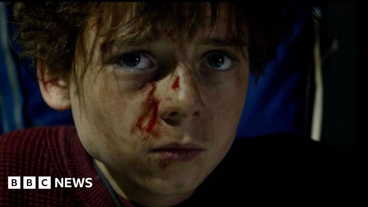 Alfie Williams is dressed as his character Spike from 28 Years Later: The Bone Temple. He looks directly into camera, and appears to be injured with blood on his face.