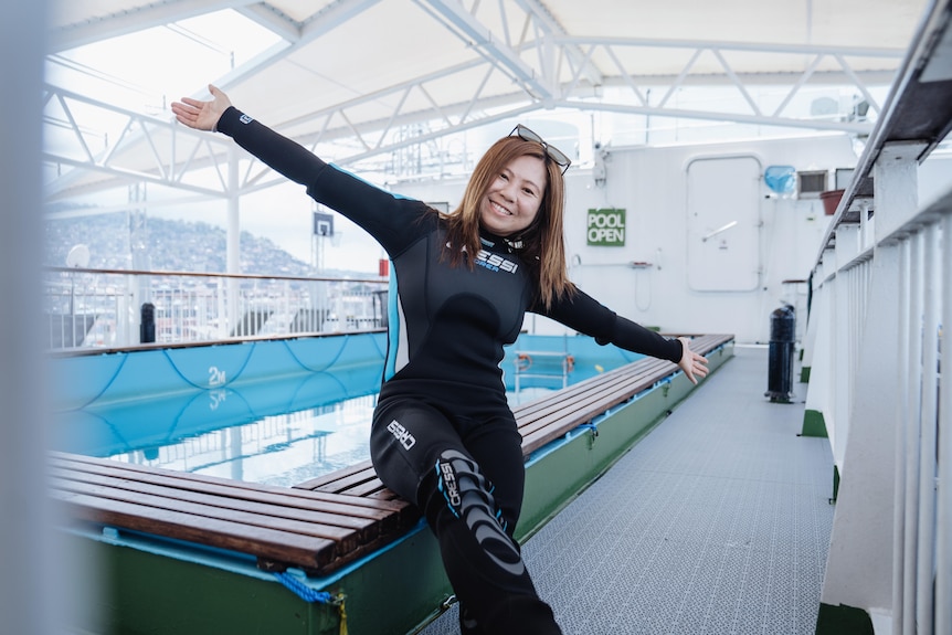 a woman in a wetsuit at a ship pool smiles at the camera