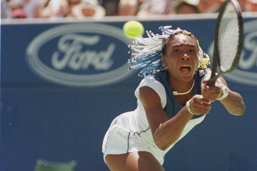 Venus Williams lunges for the tennis ball with her racket extended and a strained look on her face. 