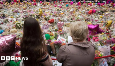 Two women stand in front of tributes to the victims of the Manchester Arena bombing in 2017