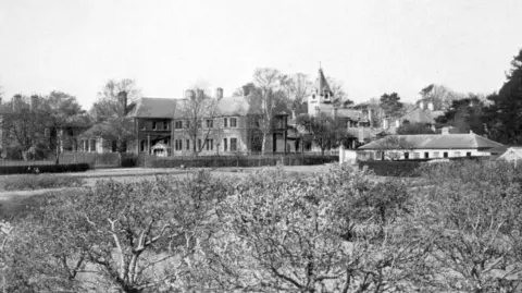 Warneford A black and white image of the hospital from the distance. A Victorian looking building can be seen from behind some bushes.