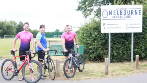 Supplied Three men pose with their bicycles at the entrance to Melbourne Sports Park.


