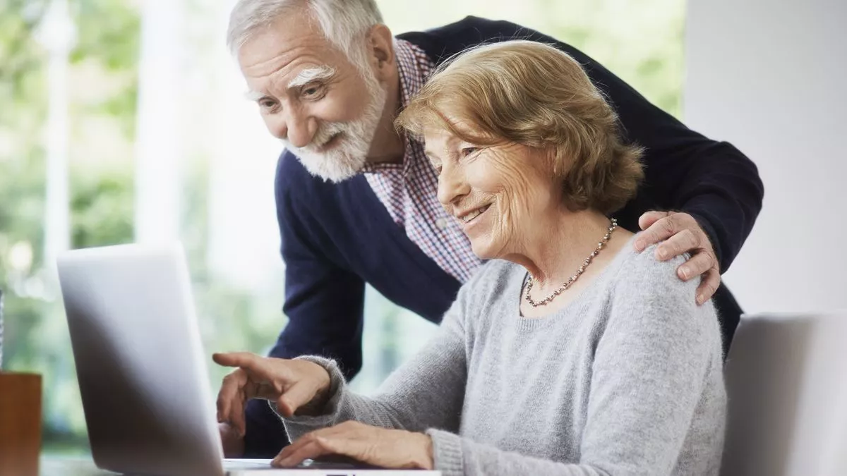 An older man and woman are looking at a computer screen 