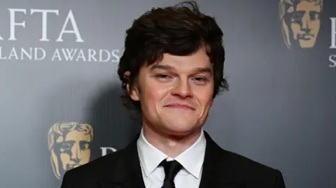 Getty Images Robert Aramayo poses in a black suit on the red carpet.