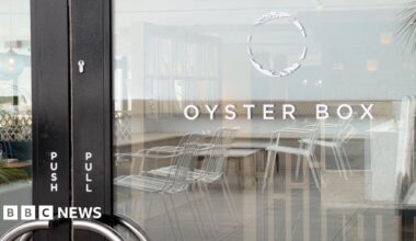 A glass door to a restaurant, with a black frame. On the glass, it says 'Oyster Box'. Above the words is a hollow white circular logo. Reflected in the glass, white metallic chairs are visible. On the black door frame are the words 'push' and 'pull' in white writing.