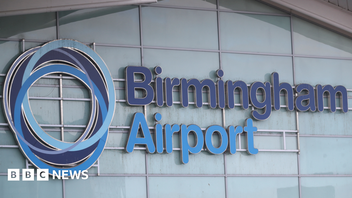 Birmingham Airport is written on the side of a building with a fogged glass exterior. The words are in dark blue and light blue lettering and there is a circular symbol to the left of the words.