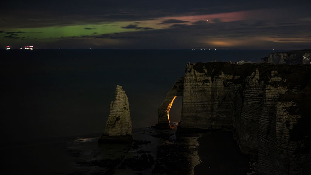 subtle green auroras peek through clouds above dramatic cliff formations.