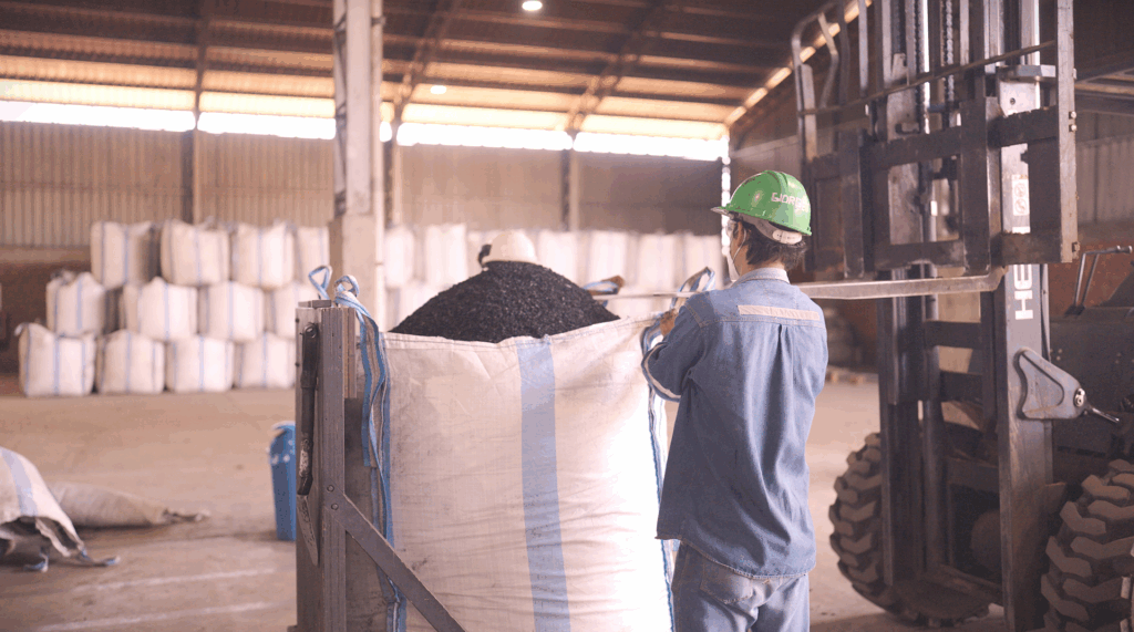 A man in a hard hat stands in front of a large bag in a warehouse.