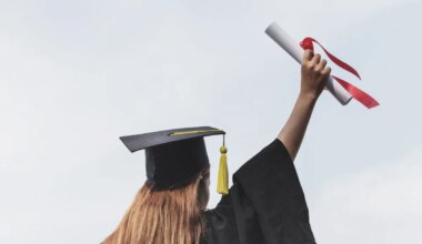 Rear view of woman in a cap and gown holding a diploma in the air.