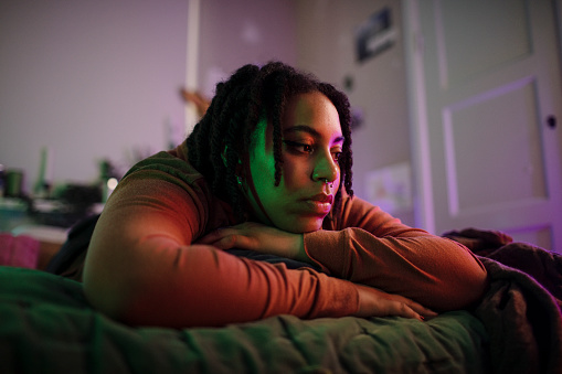 Thoughtful sad non-binary person lying on bed at home