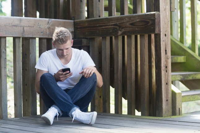 Young man using mobile phone on floorboard, Freiburg im Breisgau, Baden-Wurttemberg, Germany