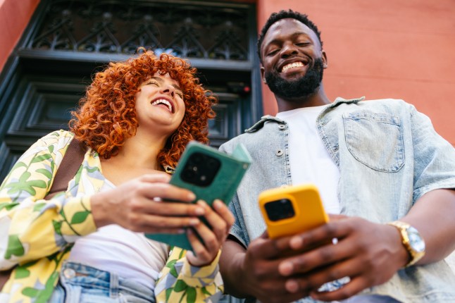 View from below of multiethnic friends using smartphones and laughing.